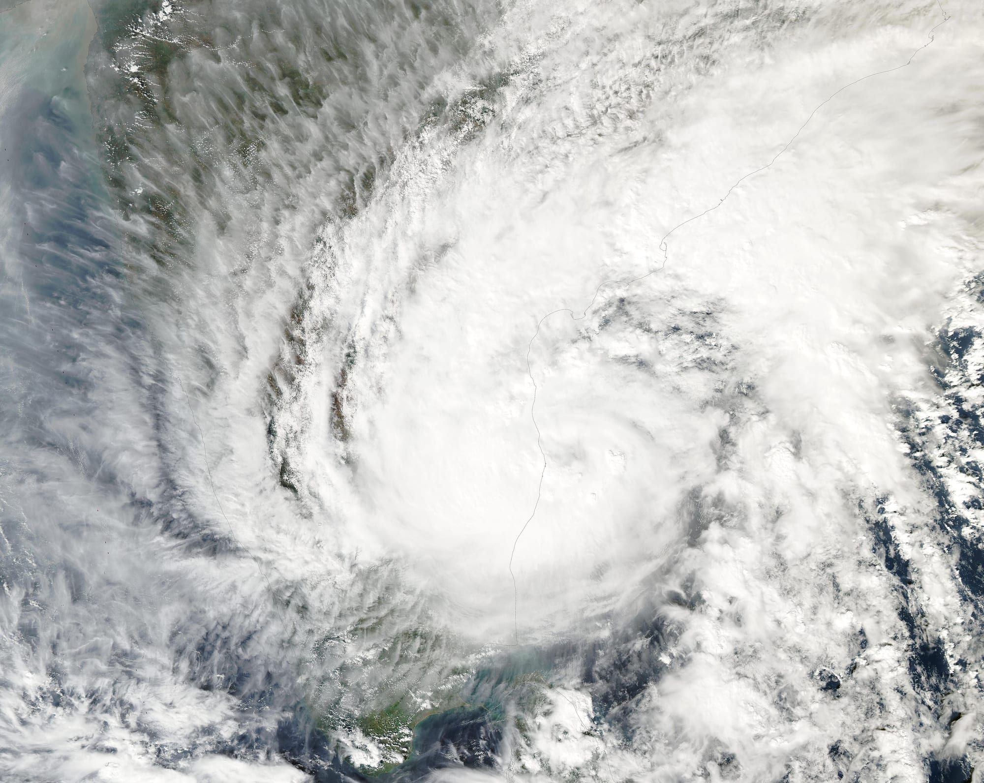 Satellite view of a large white spiral cloud mass, a tropical cyclone, over the sea with the Indian coastline at its edge.