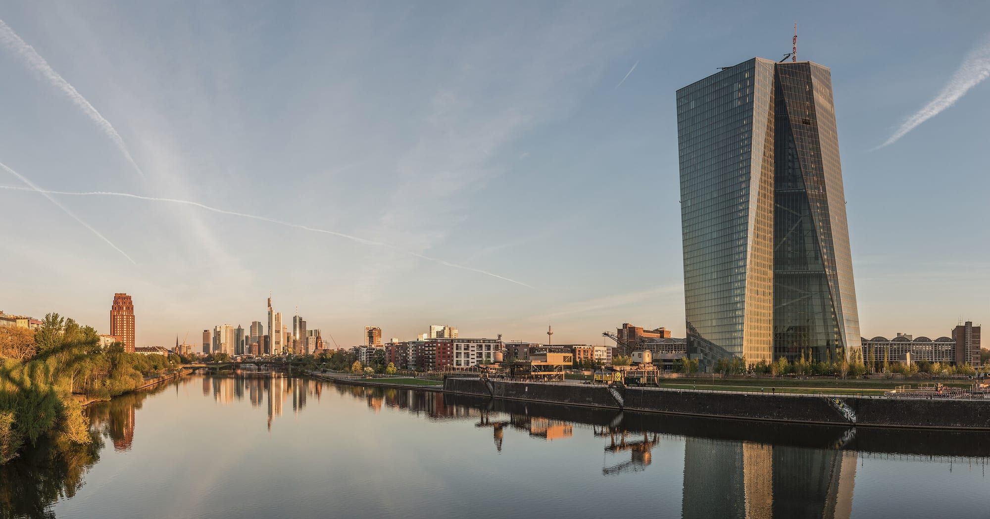 La tour de verre du siège de la Banque centrale européenne se reflète dans le Main, à l'aube, avec les gratte-ciel de Francfort à l'horizon.