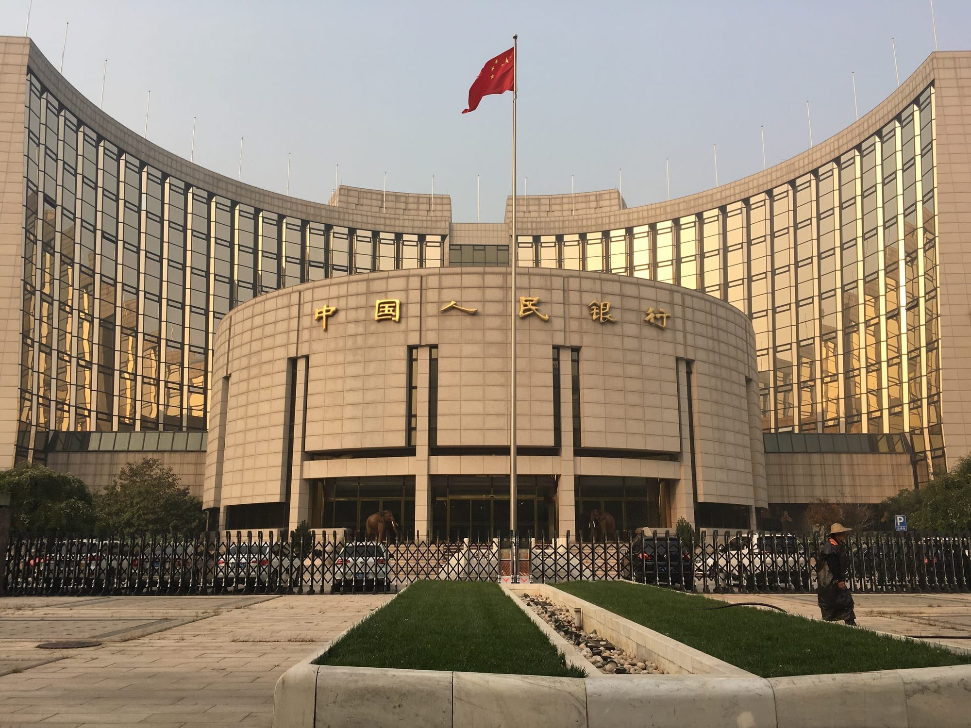 北京中国人民银行总部大楼，弧形的玻璃幕墙立面前方，旗杆上飘着一面红旗。