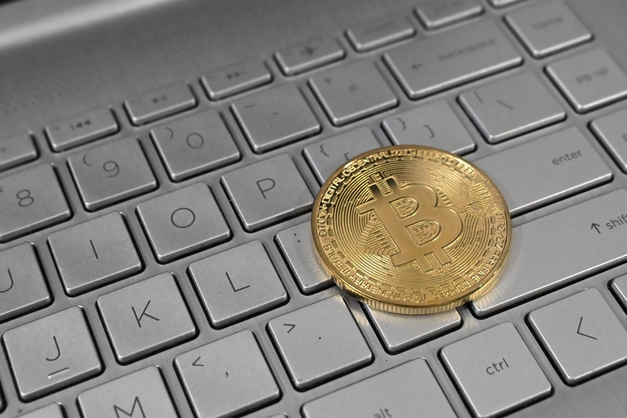 Une pièce dorée frappée du logo du bitcoin posée sur le clavier gris d'un ordinateur portable.